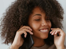 Chica de color con rizos escuchando un mensaje en su celular